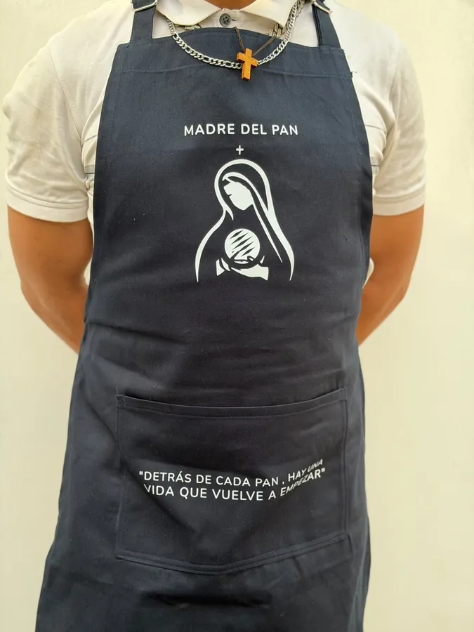 Delantal azul de Madre del Pan con el logo y la frase «Detrás de cada pan, hay una vida que vuelve a empezar»