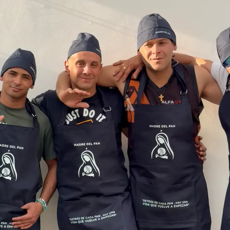 Cuatro integrantes del equipo de Madre del Pan, con delantal y gorro de la panadería, saludan abrazados